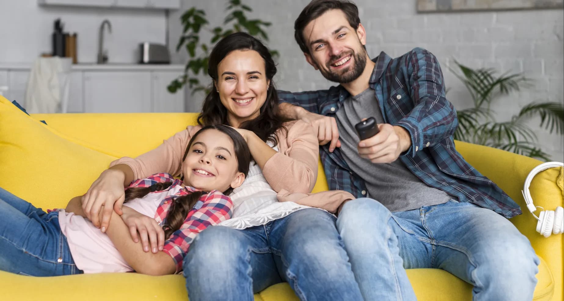 Familia sonriendo en un sofá amarillo en casa, representando protección y tranquilidad con Seguro Vehicular Touring